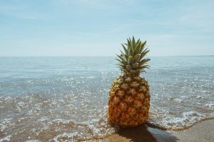 A pineapple sits at the edge of the waves and sand.